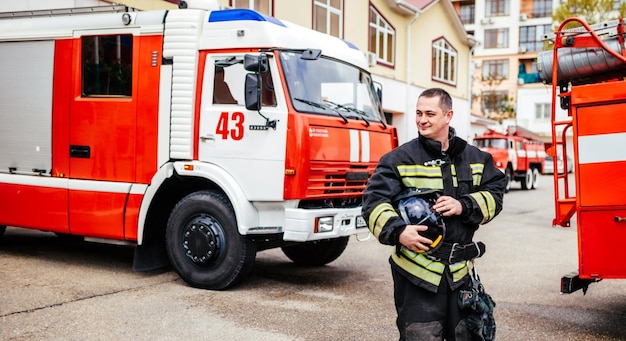 Homem de bombeiros em um traje de proteção perto de caminhão de bombeiros Resgate de proteção do perigo Corpo de bombeiros