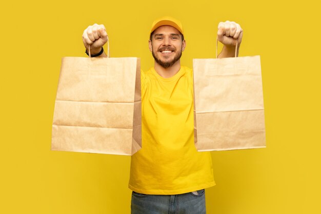 Homem de boné amarelo, camiseta dando pacotes de papel isolados. mensageiro empregado segurando pacotes de papel com comida