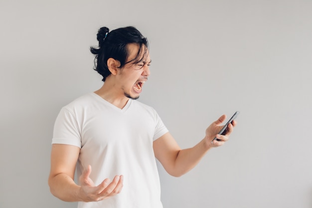 Homem de cabelo comprido com raiva e furioso em t-shirt branca está usando o smartphone.