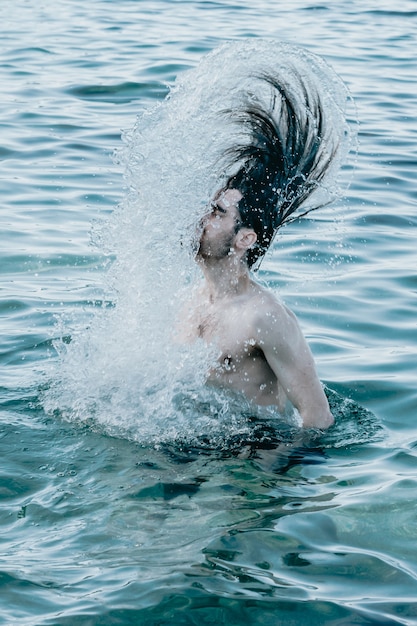 Homem de cabelo comprido dentro de água cristalina refrescando seu cabelo, água cristalina, conceito de férias