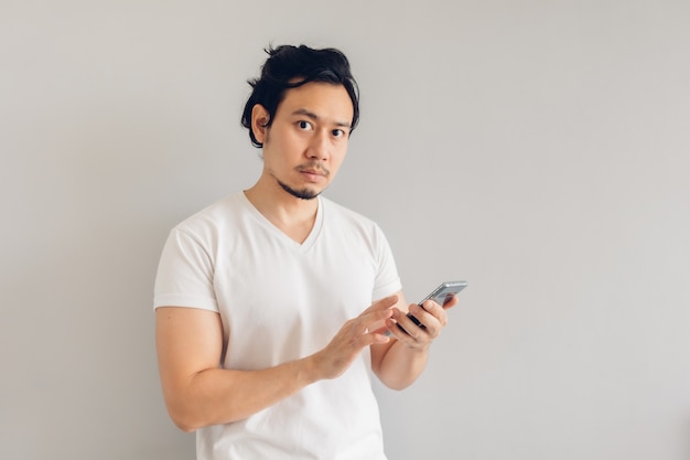 Homem de cabelo comprido em uma camiseta branca casual está usando o smartphone.