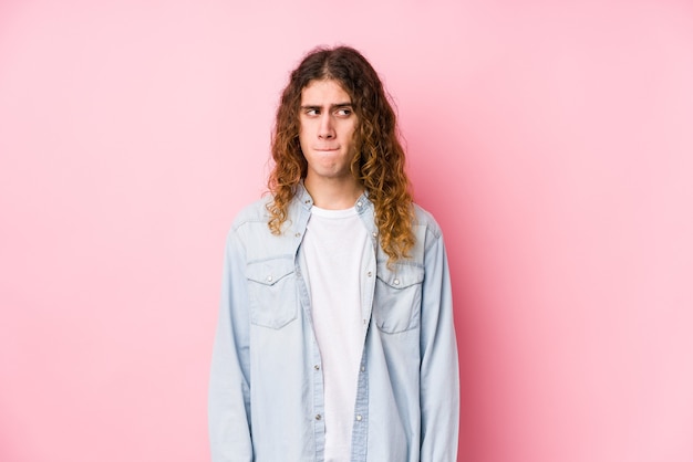 Homem de cabelo comprido posando isolado, confuso, sente-se em dúvida e inseguro.