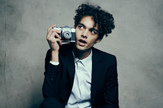 Homem de cabelo encaracolado em uma jaqueta e camisa segurando uma câmera na mão modelo estilo vogue