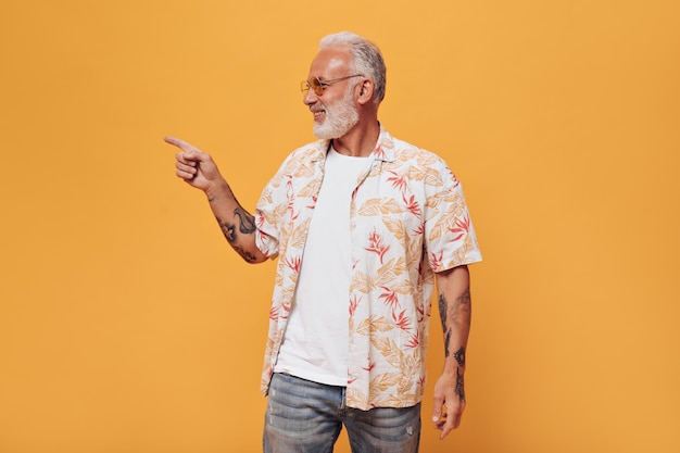 Homem de cabelos brancos na camisa da planta apontando para o lugar para texto em fundo laranja Adulto em camiseta branca camisa de verão e jeans azul está sorrindo