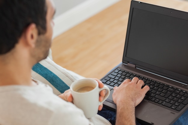 Homem de cabelos castanhos segurando café usando seu laptop