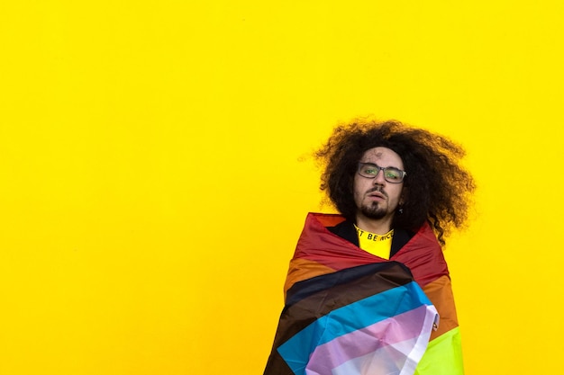 Homem de cabelos compridos envolto em bandeira de orgulho de progresso intersexclusivo em fundo amarelo