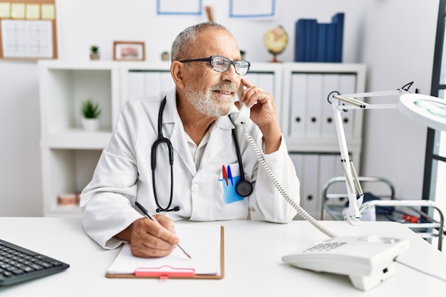 Homem de cabelos grisalhos sênior vestindo uniforme médico falando ao telefone na clínica