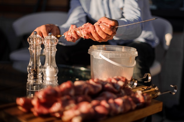 Homem de camisa azul amarra um pedaço grande de carne fresca no espeto