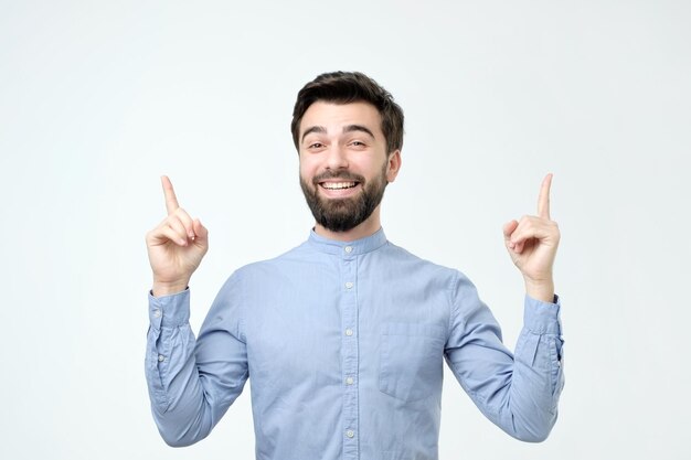 Homem de camisa azul, apontando para cima com o dedo isolado no fundo cinza