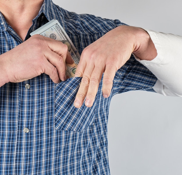 Foto homem de camisa azul coloca em um bolso uma pilha de papel-moeda