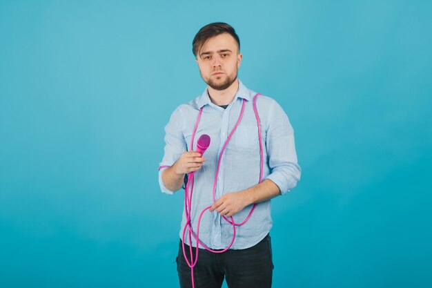 homem de camisa azul fica em fundo azul e canta no microfone rosa