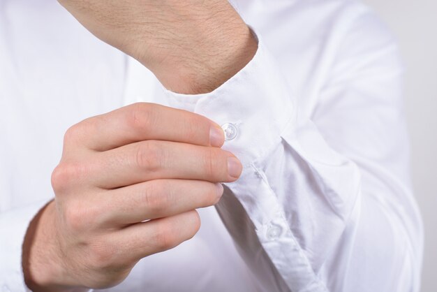 Homem de camisa branca com os dedos desabotoando o botão