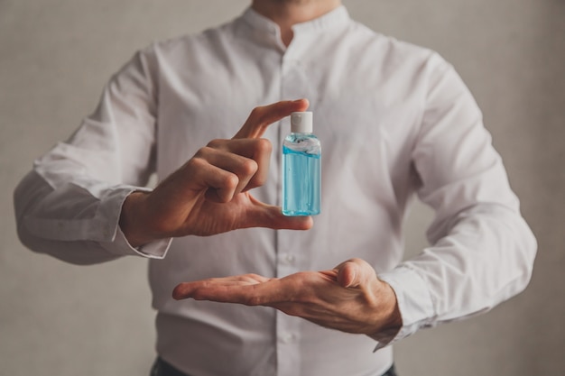 Homem de camisa branca detém desinfetante de gel de álcool. Foco seletivo.