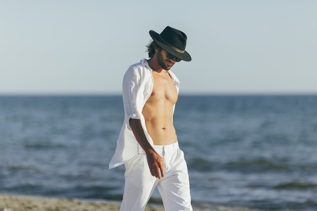 Homem de camisa branca e calça com chapéu preto na praia