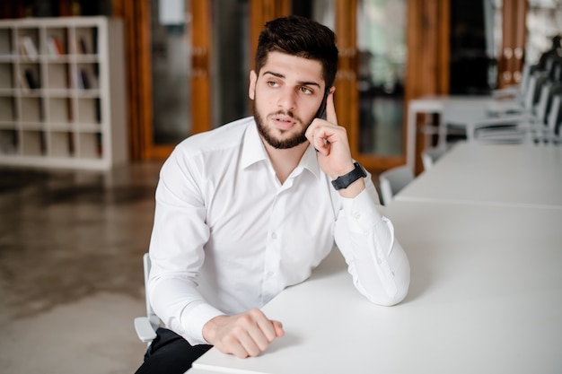 Homem de camisa branca, falando ao telefone no escritório