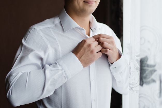 homem de camisa branca noivo abotoa sua camisa camisa branca no dia do casamento