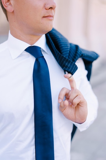 Homem de camisa branca segurando uma jaqueta pendurada no ombro com o dedo