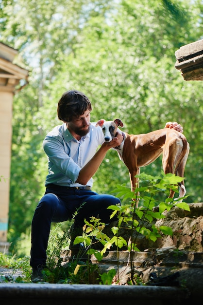 Homem de camisa e calça sentado em um parque olhando para o cachorro