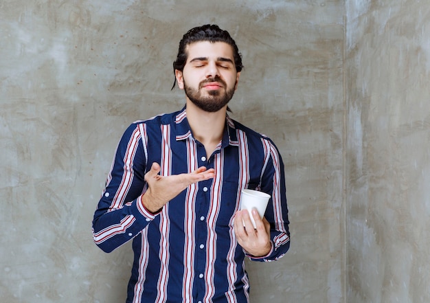 Homem de camisa listrada segurando um copo d'água descartável branco e sentindo o cheiro