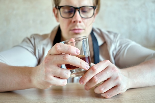 Homem de camisa, olhando para um copo de álcool