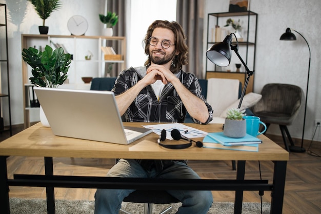 Homem de camisa quadriculada e óculos sentado à mesa com laptop moderno