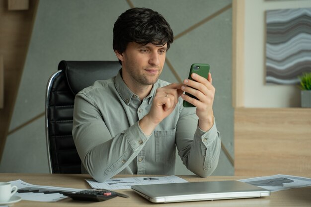 Homem de camisa, sentado em um escritório e usando um smartphone para o trabalho