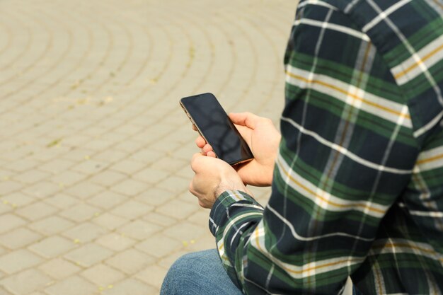 Homem de camisa usando smartphone sentado no parque