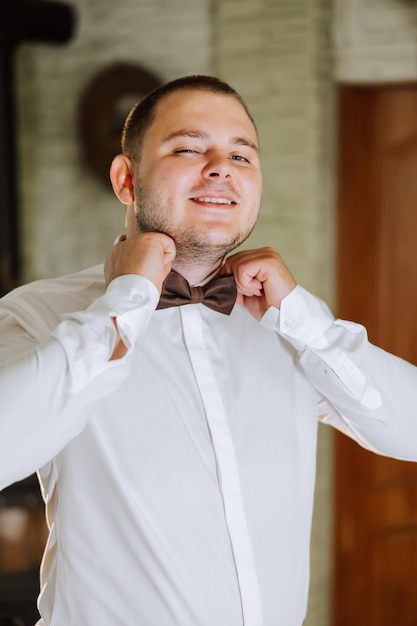 Foto homem de camisa vestindo-se e ajustando gravata no pescoço em casa conceito de dia de casamento moda estilo de negócios masculino