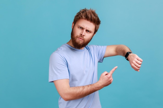 Homem de camiseta azul, apontando o dedo em seu relógio de pulso, verificando impacientemente o prazo atrasado