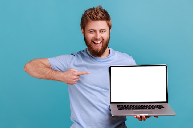 Homem de camiseta azul segurando laptop e apontando para a tela vazia sorrindo satisfeito com o aplicativo de computador