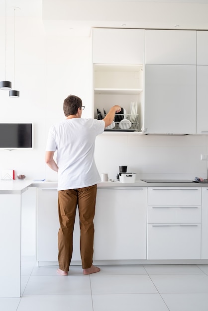 Homem de camiseta branca lavando pratos na cozinha