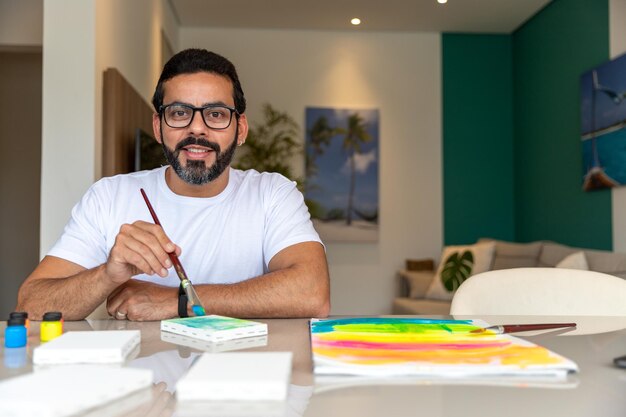 homem de camiseta branca praticando arte-terapia em tela de pintura com tintas coloridas com um pincel