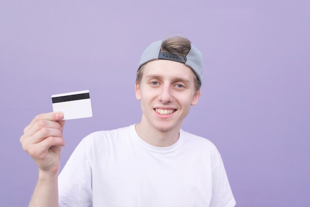 Homem de camiseta branca tem um cartão bancário nas mãos e sorri sobre um fundo roxo