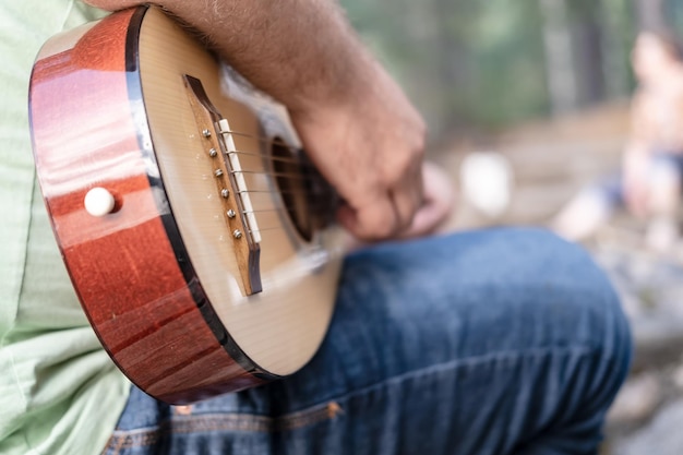 Foto homem de camiseta e jeans toca violão em um fundo desfocado