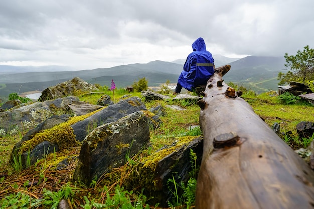 Homem de capa de chuva sentado em um tronco na floresta enquanto chove incessantemente