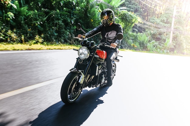 Homem de capacete anda de bicicleta na estrada entre trópicos de verão e olha para a câmera