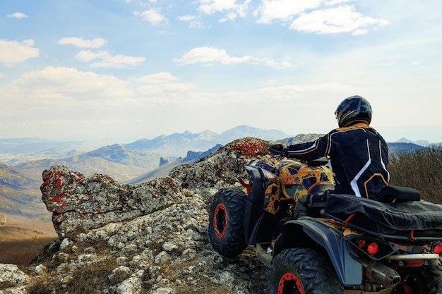 Homem de capacete sentado em um quadriciclo ATV nas montanhas