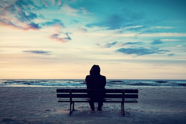 Homem de capuz sentado em um banco solitário na praia