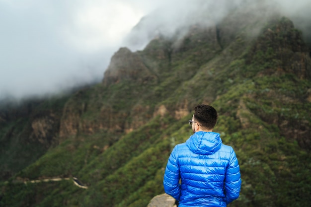 Homem de casaco azul relaxante nas montanhas com céu nublado