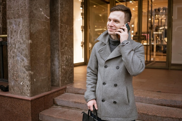 Homem de casaco cinza e suéter fica na rua da cidade Fala ao telefone Resolve