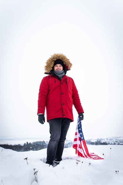 Homem de casaco de inverno vermelho segurando a bandeira dos eua ao ar livre em tempo de neve