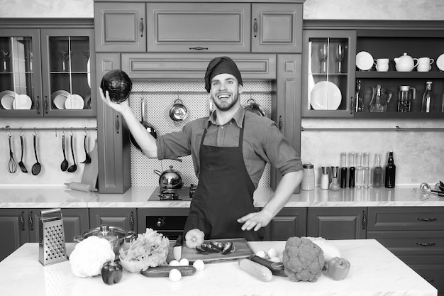 Homem de chapéu de chef sorri com repolho roxo na cozinha