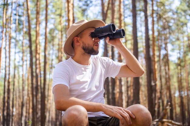 Homem de chapéu olha através de binóculos durante uma viagem de acampamento Caminhada na floresta de montanhas