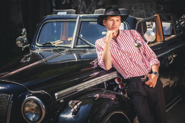 Foto homem de chapéu preto clássico em pé perto de carro antiquado