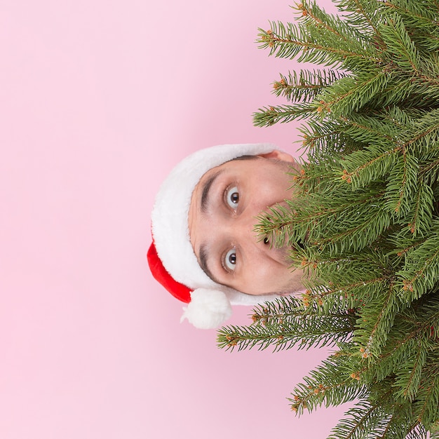 Homem de chapéu vermelho espreita por trás das árvores de Natal