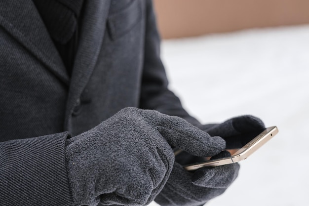 Homem de colheita em tela sensível ao toque de luvas e usando smartphone em tempo frio no inverno na cidade