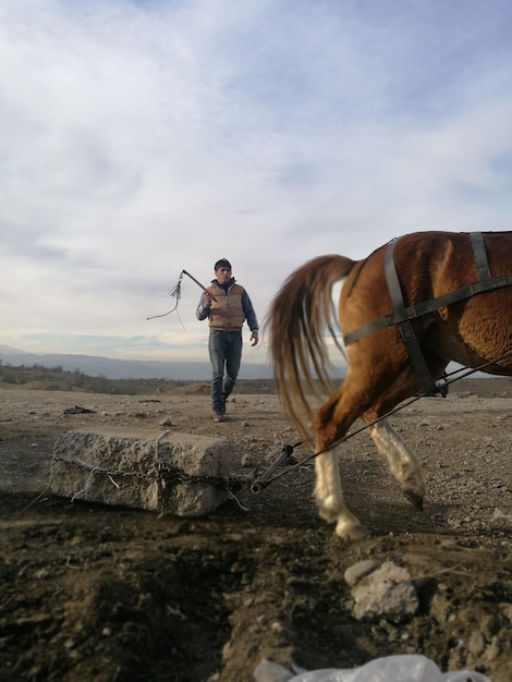 Homem de comprimento completo com cavalo caminhando no campo contra o céu nublado