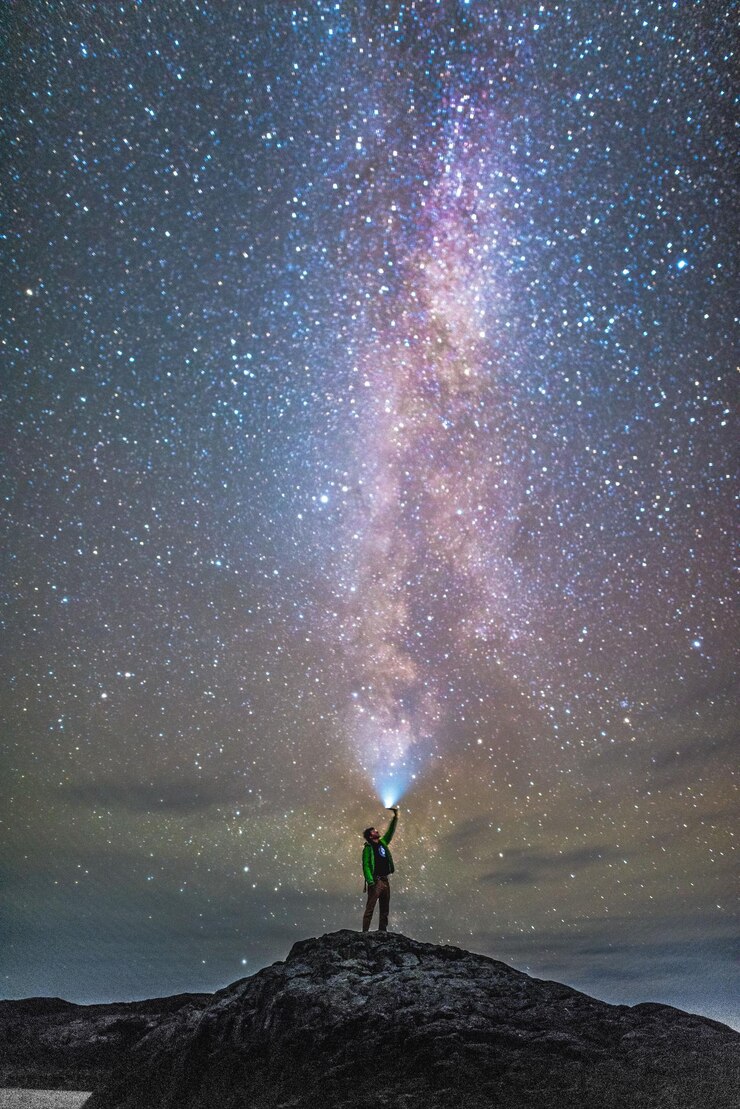 Foto homem de comprimento completo com lanterna de pé na rocha contra o céu à noite