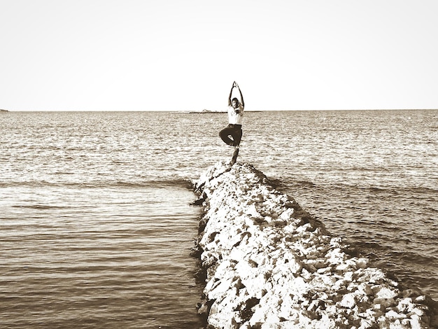 Foto homem de comprimento completo fazendo ioga na virilha contra o mar na praia