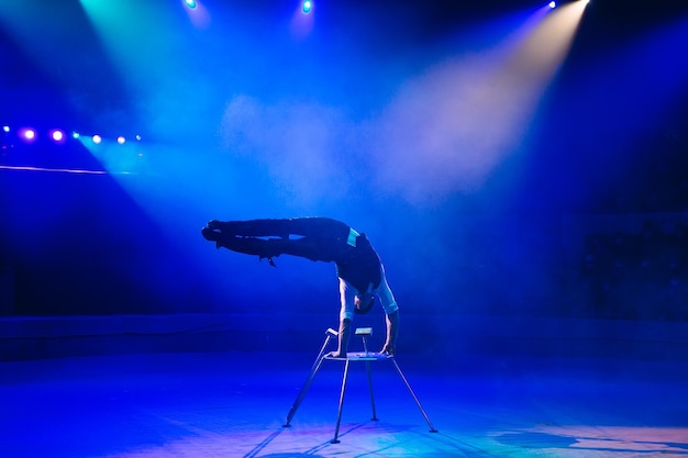 Homem de constituição atlética realiza exercícios de ginástica complexos na arena do circo